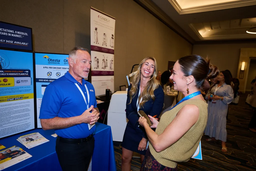 Three conference participants chatting beside an Otezla exhibitor display at Sunrise NPPA Derm.