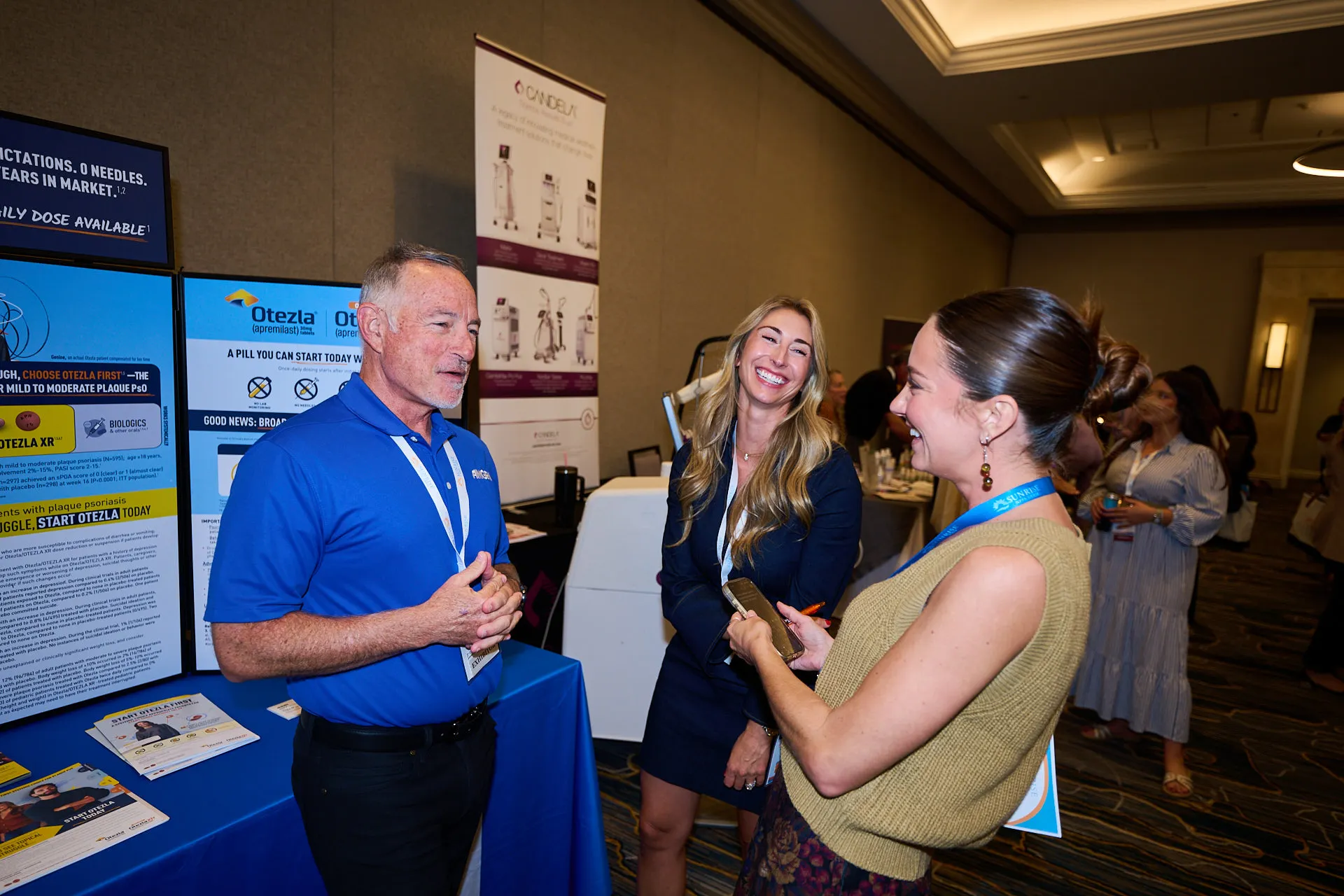 Three conference participants chatting beside an Otezla exhibitor display at Sunrise NPPA Derm.