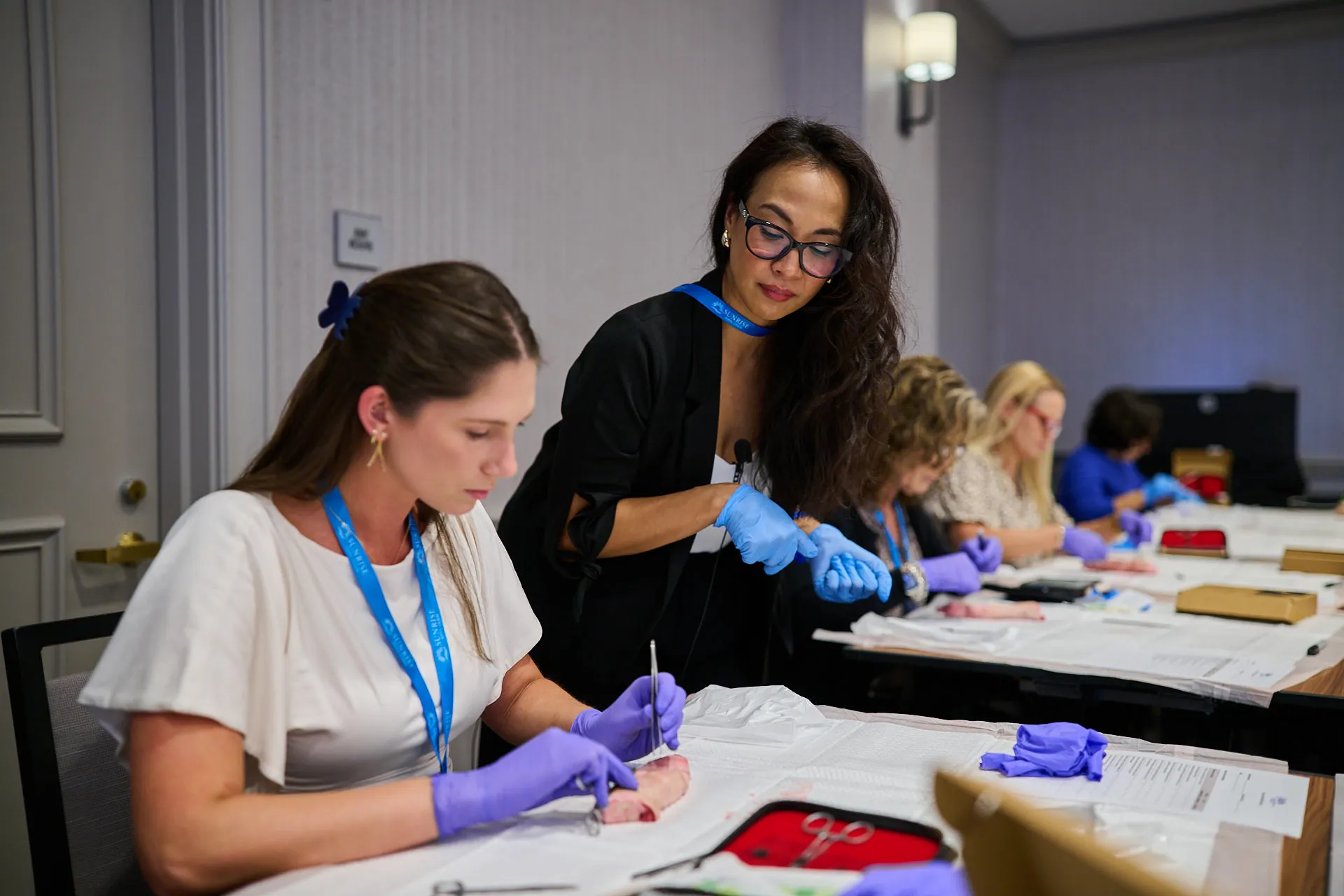 Instructor guiding an attendee practicing a procedure on a training model during a Sunrise NPPA Derm workshop.