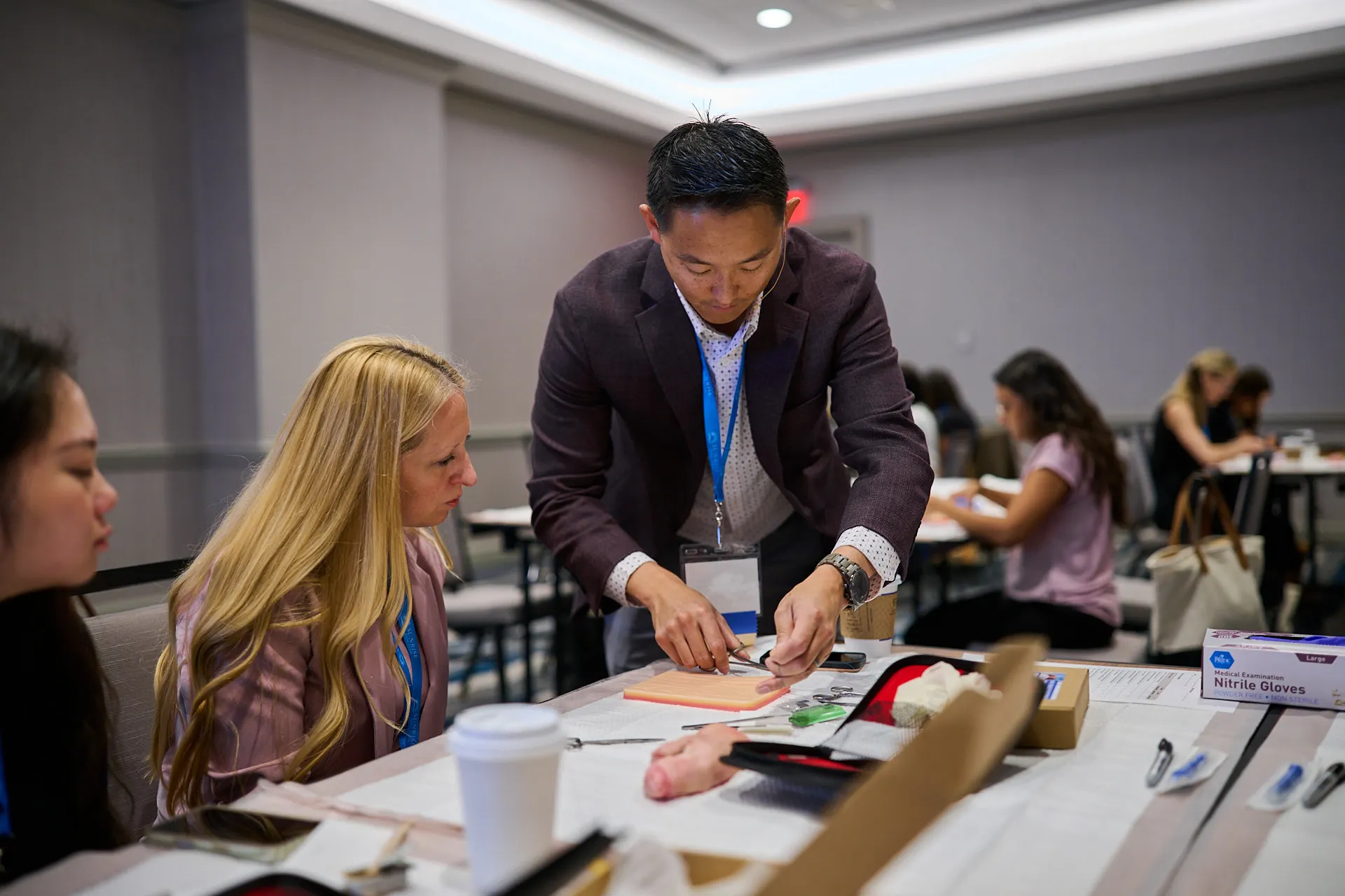 Instructor demonstrating suturing on a training pad as attendees watch during a Sunrise NPPA Derm workshop.